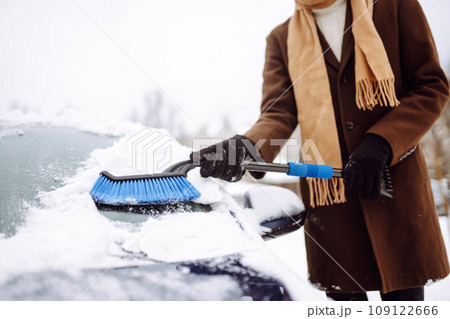 Stylish man in a coat and scarf clears snow from his car during winter snowfall. Seasonality concept Stylish man in a coat and scarf clears snow from his car during winter snowfall. Seasonality concept 109122666
