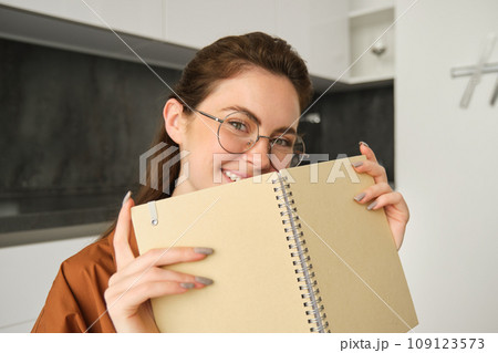 Close up portrait of young woman smiling, holding notebook, showing her planner 109123573