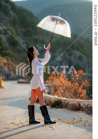 woman umbrella leaves , She holds him over her head, autumn leaves are falling out of him. Beautiful woman in a dress with an umbrella in the autumn park on the road in the mountains. 109123940