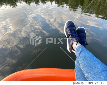 Legs on the edge of the catamaran, copy space. Person dangling down the feet above water. Concept of leisure on nature 109124917