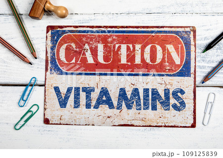 Vitamins. Metal CAOTION plate with text on a white wooden background 109125839