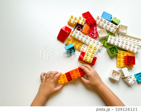 Child playing with colorful building blocks on white background. Top view 109126121