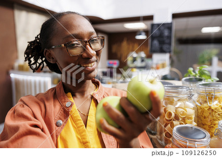 POV of an African American woman promoting eco friendly, organic products like green apples, at a local supermarket. Fresh, nutritious food items are showcased in glass jars. POV of an African American woman promoting eco friendly, organic products like green apples, at a local supermarket. Fresh, nutritious food items are showcased in glass jars. 109126250