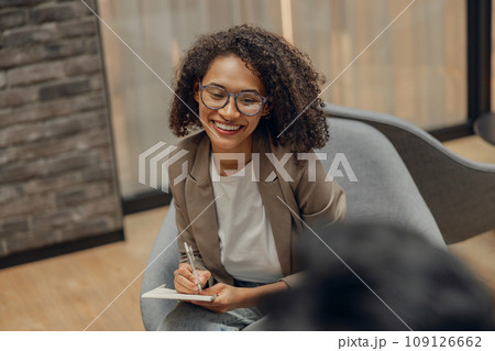Smiling woman writing something down while sitting with colleague in modern office 109126662
