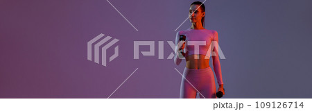 Attractive fitness woman doing exercises with dumbbells on studio background with colored filter 109126714
