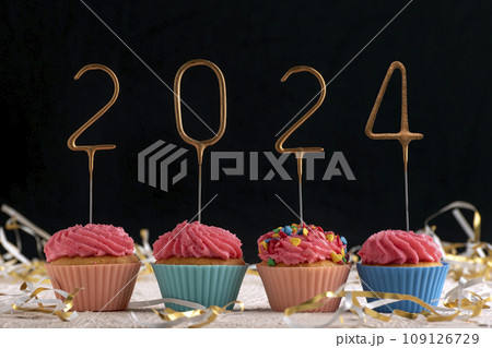 Holiday cupcake with pink glaze and 2024 numbers on black background. New Year and Christmas. 109126729