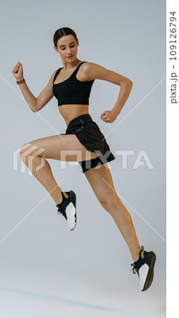 Pretty sporty woman running in Mid-Air exercising during cardio workout over studio background 109126794