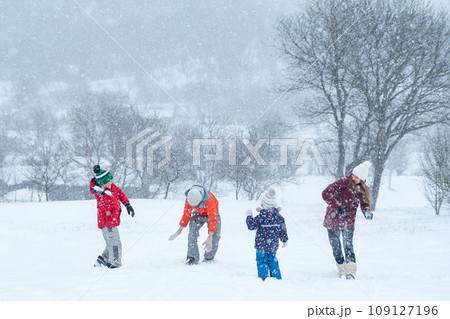 Big family with children play snowballs outside during snowfall. Winter fun holidays. Games in winter outdoors. 109127196