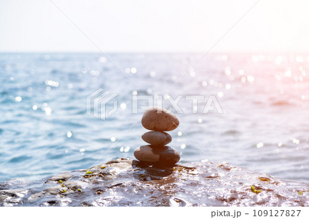 Balanced rock pyramid on sea pebbles beach, sunny day and clear sky at sunset. Golden sea bokeh on background. Selective focus, zen stones on sea beach, meditation, spa, harmony, calm, balance concept Balanced rock pyramid on sea pebbles beach, sunny day and clear sky at sunset. Golden sea bokeh on background. Selective focus, zen stones on sea beach, meditation, spa, harmony, calm, balance concept 109127827