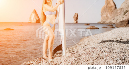 Woman sea sup. Close up portrait of happy young caucasian woman with long hair looking at camera and smiling. Cute woman portrait in a blue bikini posing on sup board in the sea Woman sea sup. Close up portrait of happy young caucasian woman with long hair looking at camera and smiling. Cute woman portrait in a blue bikini posing on sup board in the sea 109127835