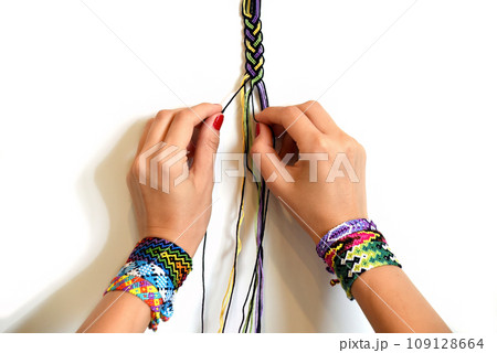 Female hands weaving knot for DIY friendship bracelet Pigtail. Many handmade bracelets on girls wrists. Friendship bracelet making process, step by step. White background with copy space Female hands weaving knot for DIY friendship bracelet Pigtail. Many handmade bracelets on girls wrists. Friendship bracelet making process, step by step. White background with copy space 109128664