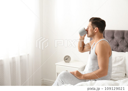 Man with cup of coffee in bedroom. Lazy morning Man with cup of coffee in bedroom. Lazy morning 109129021