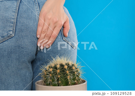 Woman sitting down on cactus against light blue background, space for text. Hemorrhoid concept Woman sitting down on cactus against light blue background, space for text. Hemorrhoid concept 109129528