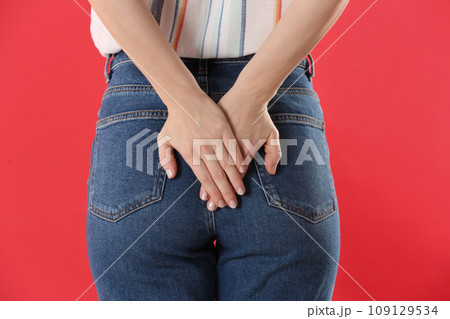 Woman suffering from hemorrhoid on red background, closeup Woman suffering from hemorrhoid on red background, closeup 109129534