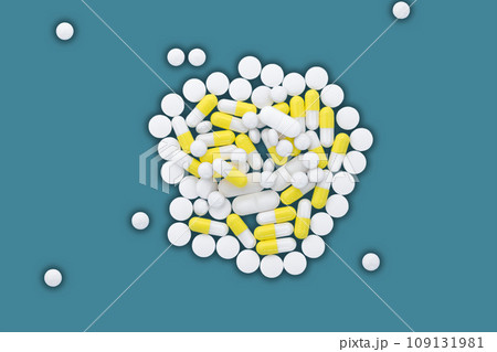 A pile of white and yellow pills lie on a blue background. 109131981