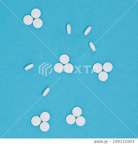 White pills on soft light pastel blue color, top view, copy space. Health and pharmacy remedies background. White pills on soft light pastel blue color, top view, copy space. Health and pharmacy remedies background. 109132003