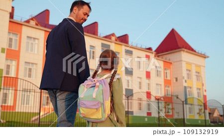 father leads his daughter hand school. happy life family. little child daughter holds happy father hand while going school house. little child and his parent go to class. school life kid with bag his 109132919