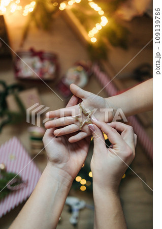 Mother put Christmas tree toy on daughter hand. Background of Christmas light and decorations. Mother put Christmas tree toy on daughter hand. Background of Christmas light and decorations. 109139786