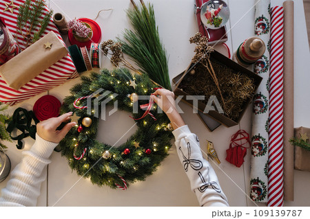 Top view of mom and daughter decorating Christmas wreath. Process of home made winter decor Top view of mom and daughter decorating Christmas wreath. Process of home made winter decor 109139787