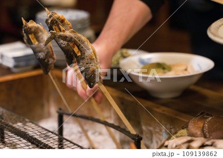 囲炉裏で魚を焼くところ　クローズアップの手元	 109139862