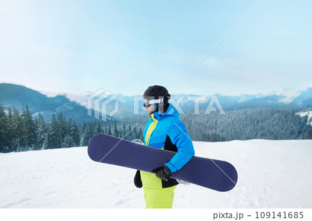 Snowboarder Of Man At Ski Resort On The Background Blue Sky,  Hold Snowboard. Wearing Ski Glasses. Ski Goggles  With The Reflection Of Snowed Mountains 109141685