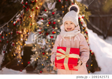 Little girl with a Christmas gift outdoors in winter on Christmas Eve. 109142571
