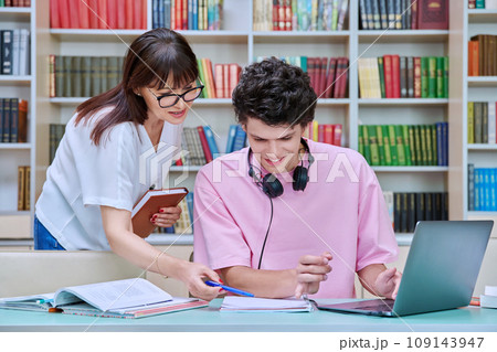Woman mentor teaching male student in college library, exam preparation Woman mentor teaching male student in college library, exam preparation 109143947