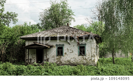 An image of a house that appears to be abandoned and neglected, surrounded by overgrown plants and a damaged roof. 109148095