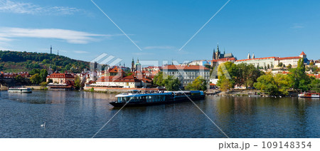 This is a photo of a river with a boat and buildings in the background. Pleasure boat on the Vltava pier in the fall. View of Prague. 109148354