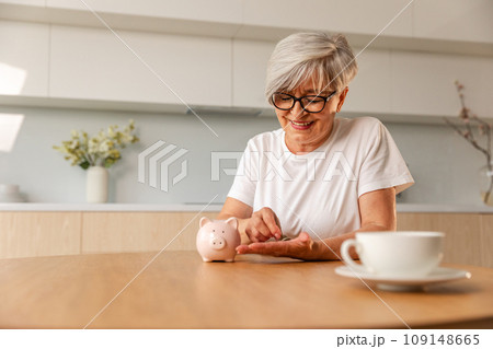 Saving money investment for future. Senior adult mature woman putting money coin in piggy bank. Old grandmother counting saving money planning retirement budget. Investment banking concept Saving money investment for future. Senior adult mature woman putting money coin in piggy bank. Old grandmother counting saving money planning retirement budget. Investment banking concept 109148665