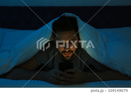 Young man addicted to smartphone in bed at night Young man addicted to smartphone in bed at night 109149079