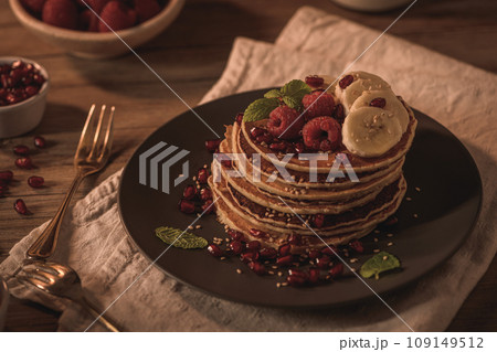 Pancakes with raspberries, banana slices, pomegranate seeds and honey 109149512