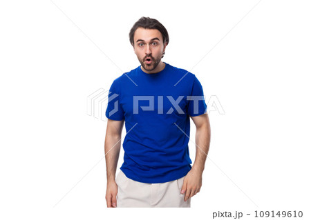 young surprised handsome european man with black hair and beard dressed in a blue t-shirt on a white 109149610
