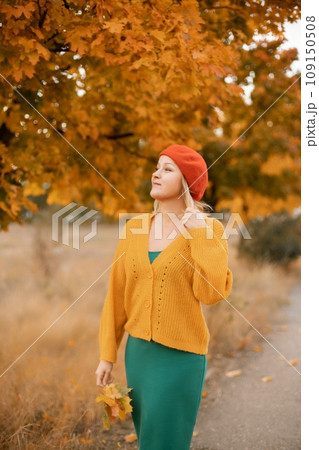 autumn woman in a red beret, yellow sweater and green skirt, against the background of an autumn tree autumn woman in a red beret, yellow sweater and green skirt, against the background of an autumn tree 109150508