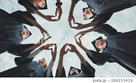 A group of college graduates stand in a circle and make hearts out of their palms. A group of college graduates stand in a circle and make hearts out of their palms. 109151419
