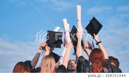 College graduates raise their caps and diplomas upward. 109151444