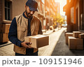 Close-up portrait of male delivery courier with cardboard box in a city street. Smiling positive Caucasian man delivering parcel to a client. Logistic and delivery concept. 109151946