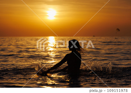 Silhouette of a girl playing with water in the sea at sunset. 109151978