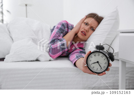 Emotional young woman with alarm clock at home in morning, focus on hand 109152163