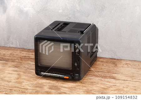 Vintage retro analog small TV set stand on wooden floor front grey concrete wall. 109154832