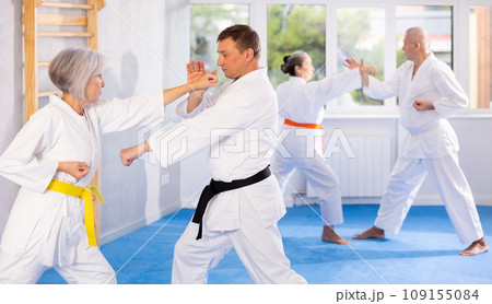 Mature women and men in pairs exercising karate movements during group training Mature women and men in pairs exercising karate movements during group training 109155084