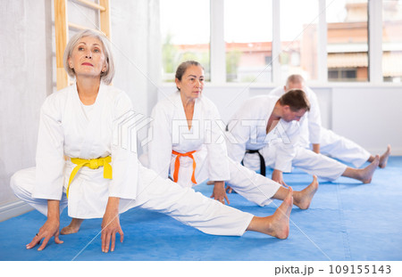 Old woman wearing kimono practicing leg stretching position in sports hall 109155143