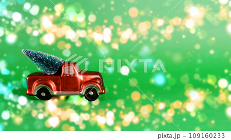 New Year card with place for text. Red car with a Christmas tree in the back of a pickup truck on a green background with blurry bokeh 109160233