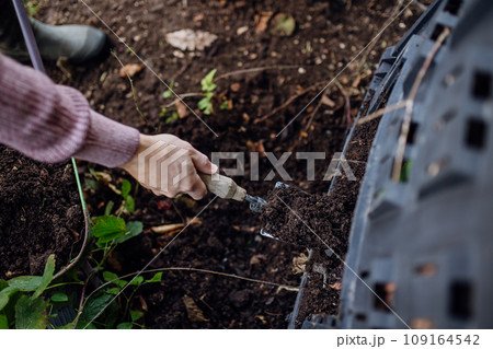 Girl removing compost from a composter in the garden. Concept of composting and sustainable organic gardening. 109164542