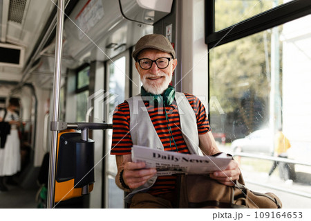 Elderly man traveling through the city by bus, reading newspaper. Senior city commuter taking tram to grocery, using public transportation. 109164653