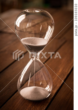 Hourglass containing white sand on a rustic wooden board 109165010