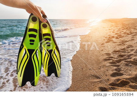 man holds flippers in his hands, against the backdrop of the sea coast. Summer sea holiday in wilderness area for snorkeling 109165894
