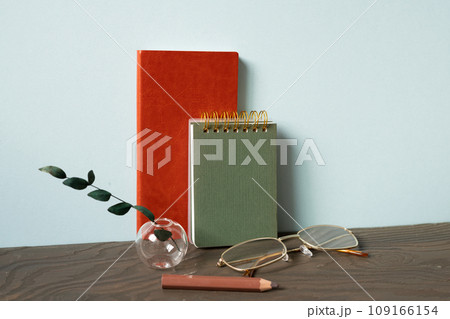 Office desk with diary note, eyeglasses, pencil, plant on wooden table. blue wall background 109166154