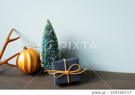 Christmas decoration ornament fir tree, golden ball, deer antler, gift box on wooden table. blue wall background 109166157
