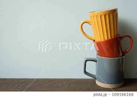 Stack of colorful ceramic mug cups on wooden table. blue wall background 109166168
